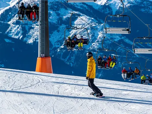 Snowboarder na stoku pod kolejką linową z narciarzami.