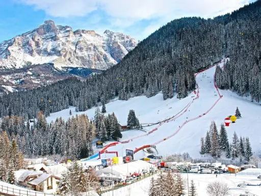 Ośnieżony stok narciarski w Alta Badia z lasem i górami w tle.