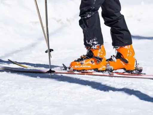 Pomarańczowe buty narciarskie Scarpa na nartach, z kijkami narciarskimi w śniegu.